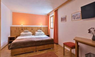 A cozy bedroom with a double bed and warm colors. Pictures hang on the wall, and a television is installed.