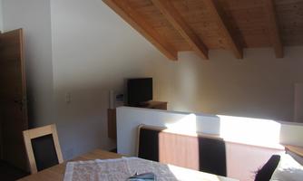 A cozy living space with wooden tables and chairs. The view of the roof beams and a television creates an inviting atmosphere.