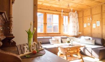 An inviting living room with wooden walls and large windows. On the table stands a decorative flower vase and a welcome sign.