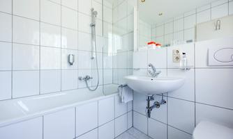 A modern bathroom with white tiles and a bathtub. There is a shower, a sink, and a toilet.