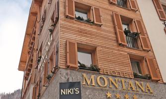A hotel building with a wooden facade and large windows. In the foreground, the entrance can be seen with a sign for the restaurant and the wine bar.