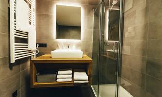 A modern bathroom with a glass shower and an elegant sink on a wooden shelf. Fresh towels and warm lighting create an inviting atmosphere.