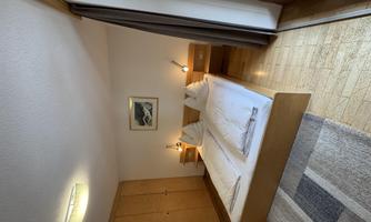 A cozy bedroom with two beds and warm wooden interiors. The large windows let in plenty of daylight.