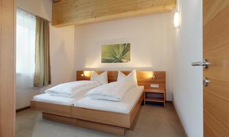 A cozy bedroom with two single beds and wooden furniture. The room has a window with curtains and modern wall decor.