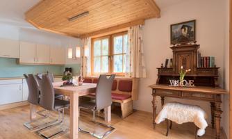 A cozy living kitchen with a wooden table and modern chairs. The window offers a view outside, and a decorative table stands beside it.