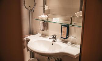A modern bathroom with a sink and a large mirror. Various care products and towels are placed on the shelf.
