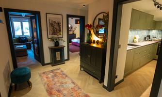 An inviting hallway with a modern design and warm colors. The kitchen is visible, and there are decorative elements like plants and artworks.