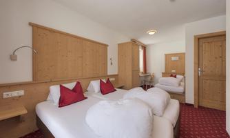A cozy hotel room with two beds and red pillows. The walls are made of wood and the floor has a red carpet.