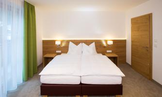 A modern bedroom with two separate beds and wooden panels. The large window front lets in plenty of daylight and creates a bright atmosphere.