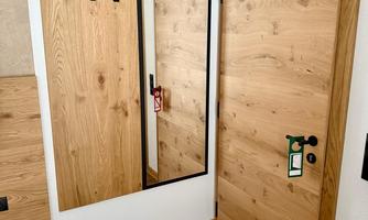 A hallway with a wooden door and a mirror. Three hooks are hanging on the wall and the floor is laid with parquet.
