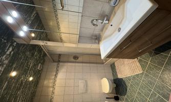 A modern bathroom with a shower and a large sink. The walls are tiled and the floor has a green color.