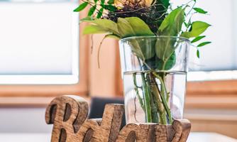 A decorative arrangement with a vase full of plants and a wooden sign that says "Relax." The table is covered with a yellow cloth.