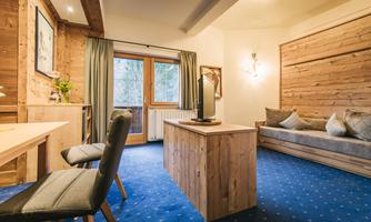 A cozy room with wooden furniture and a blue carpet. Large windows ensure plenty of daylight.