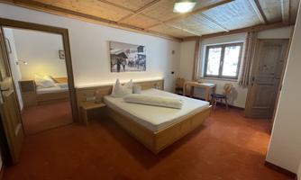 A cozy room with a double bed and wooden ceiling. The room is bright and pleasantly decorated, with a window and a small desk.
