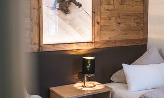 A cozy room with two beds and a wooden wardrobe. On the wall hangs a picture of a skier in the snowy mountain landscape.