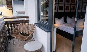 A cozy balcony with a modern chair and a small table. In the background, a bedroom with white cushions can be seen.