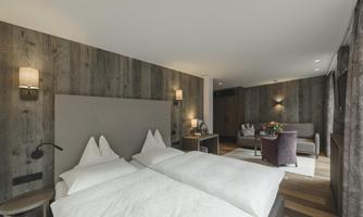 A modern hotel room with two separate beds and warm wood paneling. There are cozy furniture and natural light.
