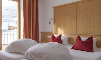 A cozy bedroom with a double bed and red cushions. The room has large windows that let in plenty of light.