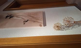 A hallway with two wooden doors and a large piece of art on the wall. On the floor stands a decorative plant with white flowers.