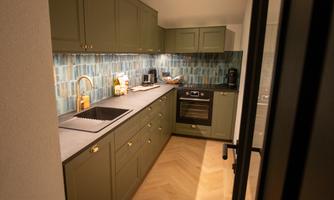 A modern kitchen with green cabinets and an elegant countertop. The walls are decorated with blue tiles.
