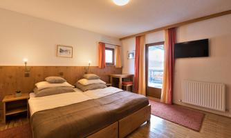 A cozy bedroom with two beds and wooden elements. A window with a view and a television on the wall complete the room.