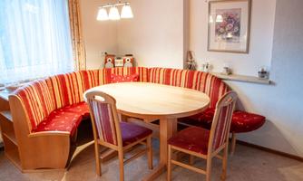 A cozy dining area with a red bench and a round table. The walls are light and adorned with a painted picture.