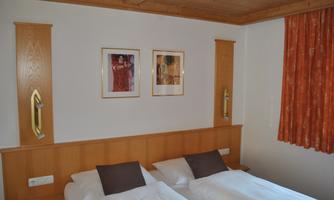 A cozy bedroom with two single beds and stylish wooden elements. On the wall hang two pictures, and an orange curtain provides a warm atmosphere.