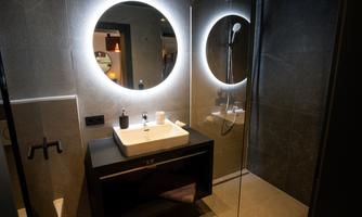 A modern bathroom with a large, illuminated mirror. The washing area is designed to be minimalist and elegant.