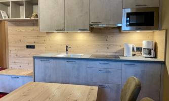 A modern kitchen with wood paneling and gray cabinets. The space is bright and inviting, featuring a dining table and kitchen appliances.