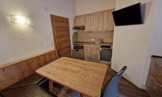 A cozy kitchen area with a wooden table and a bench. The kitchen is modernly furnished with wooden cabinets and appliances.