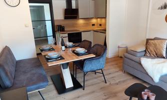A modern living room with a cozy seating area and a dining space. The kitchen is open and well-equipped, and there is a warm, inviting wooden floor.