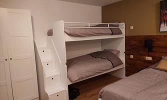 A modern bedroom with a bunk bed and a single bed. The walls are painted in soft colors, and there is a large wardrobe.