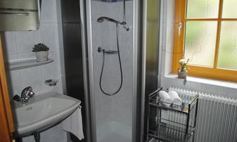 A small bathroom with a shower and a sink.  
Windows with natural light and towels on a shelf.