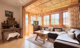 A cozy living room with wood paneling and large windows. The room is furnished with a sofa, a coffee table, and a vintage desk.