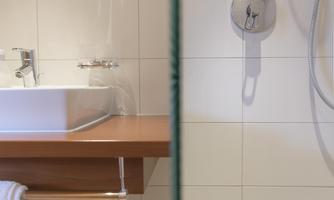A modern bathroom with a sink and a shower. The walls are tiled in light colors and the floor has appealing patterns.