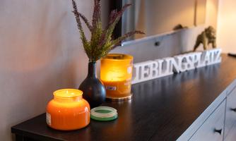 A stylish sideboard with two candles, a black vase with plants, and a decorative inscription. The warm light creates a cozy atmosphere.
