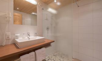 A modern bathroom with a glass shower partition and a stylish sink. Bright tiles and wooden ceilings give it a warm atmosphere.