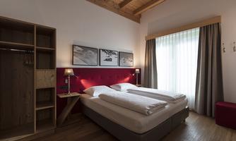 A modern bedroom with a double bed and wooden ceilings. Large windows let in plenty of light.