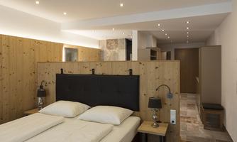 A modern bedroom with a comfortable double bed and warm wooden walls. Soft lighting creates an inviting atmosphere.