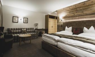 A cozy hotel room with a large double bed and a sofa. The walls are made of wood and the lighting is warm and inviting.