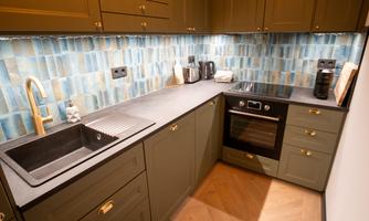 A modern kitchen with green cabinets and a stylish wall covering in shades of blue. It is equipped with a sink, an oven, and various kitchen appliances.