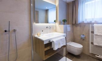 A modern bathroom with a bright sink and a large mirror. There is a shower, towels, and soft lighting.