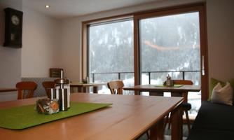 A cozy room with wooden tables and chairs. Large windows offer a view of snow-covered mountains.