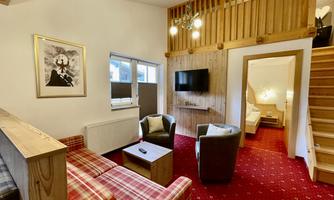 A cozy living space with red carpet and a wooden staircase. Two comfortable armchairs and a sofa invite you to relax.