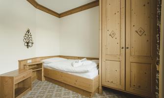 A simple room with light wooden furniture and a single bed. The walls are neutral and the decor is minimalistic.