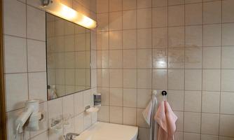 A modern bathroom with tiled wall design and wooden ceiling. It includes a sink, a mirror, towels, and a doormat.