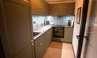 A modern kitchen with green cabinets and a light wooden floor. The walls are decorated with blue tiles and the kitchen is well equipped.