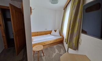 A simple room with a bed, a small table, and a television. The windows let in a lot of light and the walls are bright.