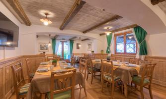 A cozy restaurant with wooden paneling and natural lighting. Tables are set, and green curtains enhance the warm atmosphere.