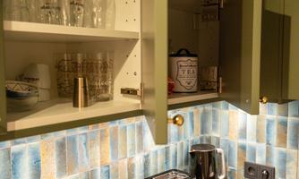 A modern kitchen with open upper cabinets, displaying glasses and dishes. On the countertop, there is a coffee maker and a toaster.